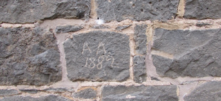 Close up of stone wall. Centre stone has 'A. A. 1882' scratched into it.
