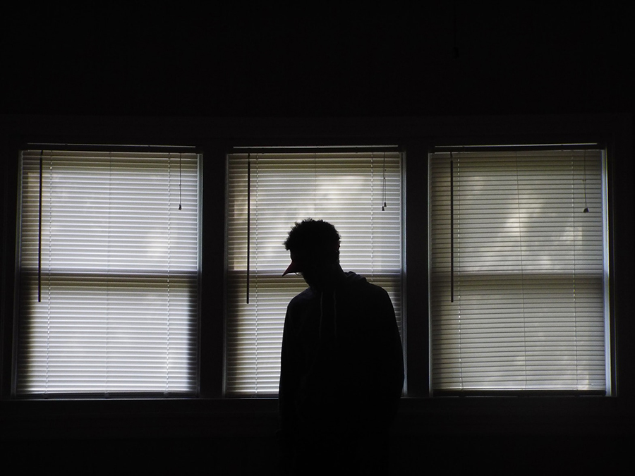 Man with a brim in silhouette standing in front of drawn blinds.
